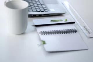 Eine Kaffeetasse, Block, Tastatur auf einem Schreibtisch.