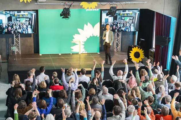 Das Bild zeigt eine Menschenmenge, die in einem Saal sitzt.