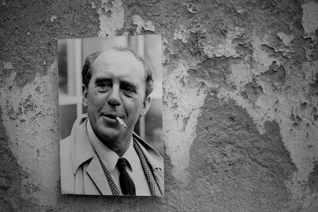 Das Bild zeigt ein Portrait von Heinrich Böll an einer strukturierten Wand.