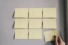 9 Post-Its an einer weißen Wand, von denen einer gerade abgehangen wird