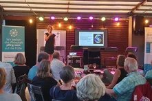 Über die Köpfe der Zuschauenden ist das Podium und die Referentin zu sehen. 