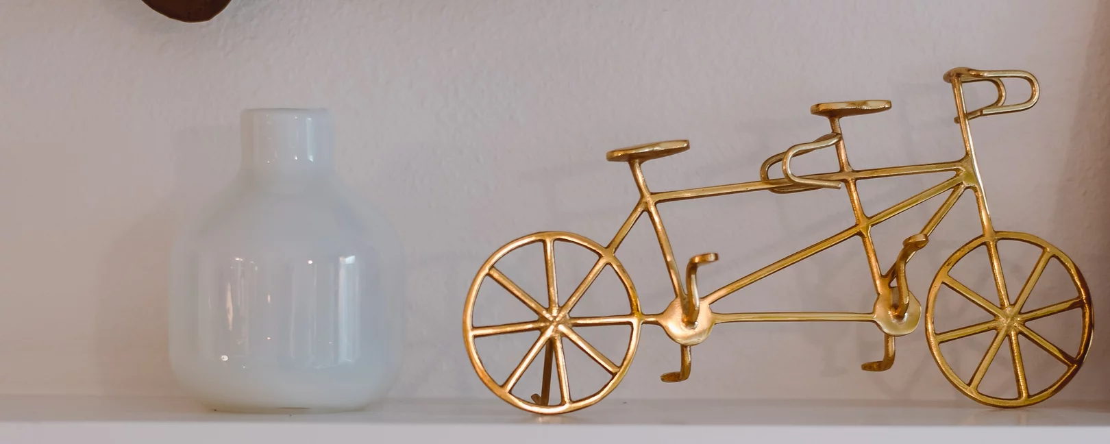 Eine goldene Figur eines Tandemfahrrads, die neben einer weißen Vase steht.