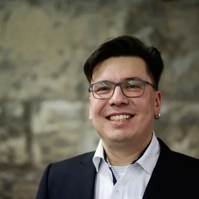 Porträt von André Moser. er steht vor einer Backsteinwand und schaut lächelnd in die Kamera.