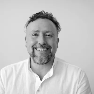 Zu sehen ist Martin Heyer. Eine männlich gelesene Person, die lächelt. Das Bild ist schwarz weiß