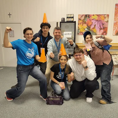 6 Personen schauen lächelnd in die Kamera, eine davon trägt ein blaues Shirt mit einem Demokratie-Fitness Logo. Weiterhin zu sehen sind orangefarbene Pylonen.