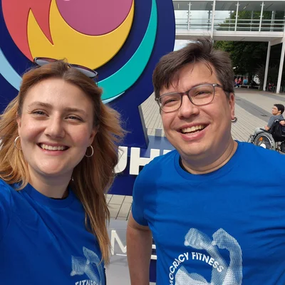 ZWei PErsonen schauen lächelnd in die Kamera, sie tragen blaue Shirts mit der Aufschrift Demokratie-Fitness.