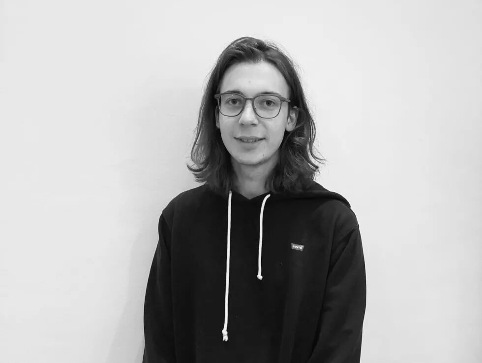 Das Bild zeigt Josef Genau, einen jungen mann mit Brille und langen Haaren sowie Sweat-Hoodie, der in die Kamera schaut.