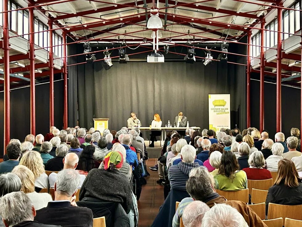 Im Hintergrund sind die Vortragenden zu sehen und im Fordergrund die Teilnehmenden