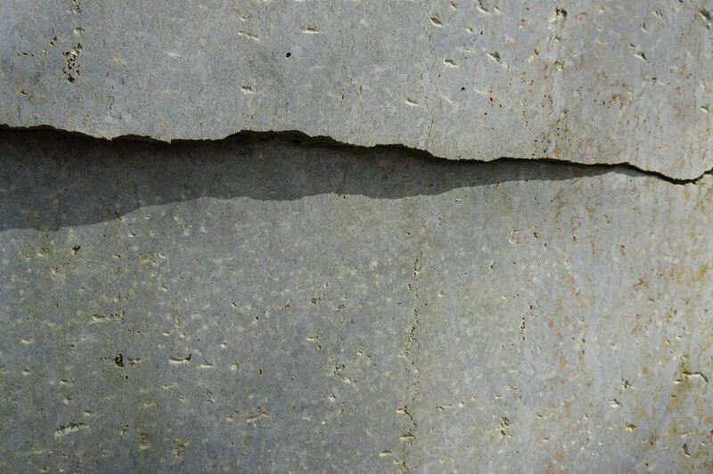 Betonwand weist einen tiefen Riss auf. Ein Schlagschatten betont ihn zusätzlich dramatisch.