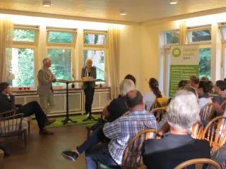 Das Bild zeigt Hermann Buschmeyer und Ulrike Burkert bei der Moderation vor dem Publikum.